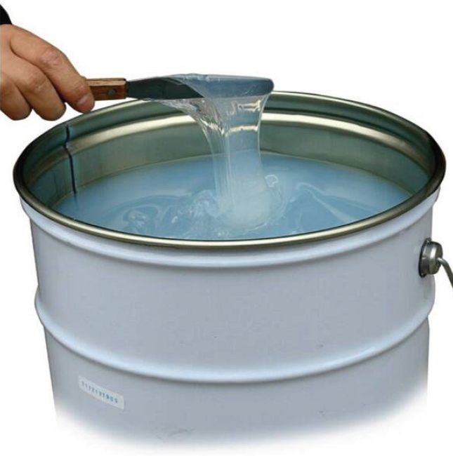 Silicone adhesive drawn from an open drum with a spatula, showing its high-stretch consistency